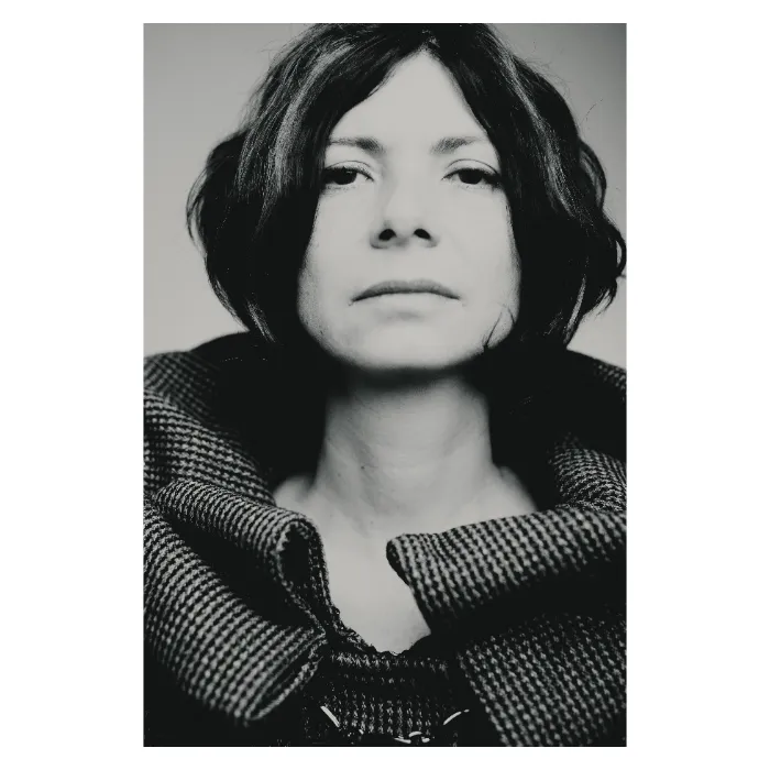 Portrait de face en noir et blanc d'une femme au regard serein, les mains relevant le col d'un manteau en maille épaisse texturée, photographie de studio épurée réalisée à Bagnolet par Nicolas Louis.