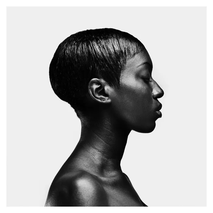 Photographie d'art de profil en noir et blanc, lignes épurées et grain de peau contrasté sur fond blanc, shooting studio Bagnolet par Nicolas Louis.