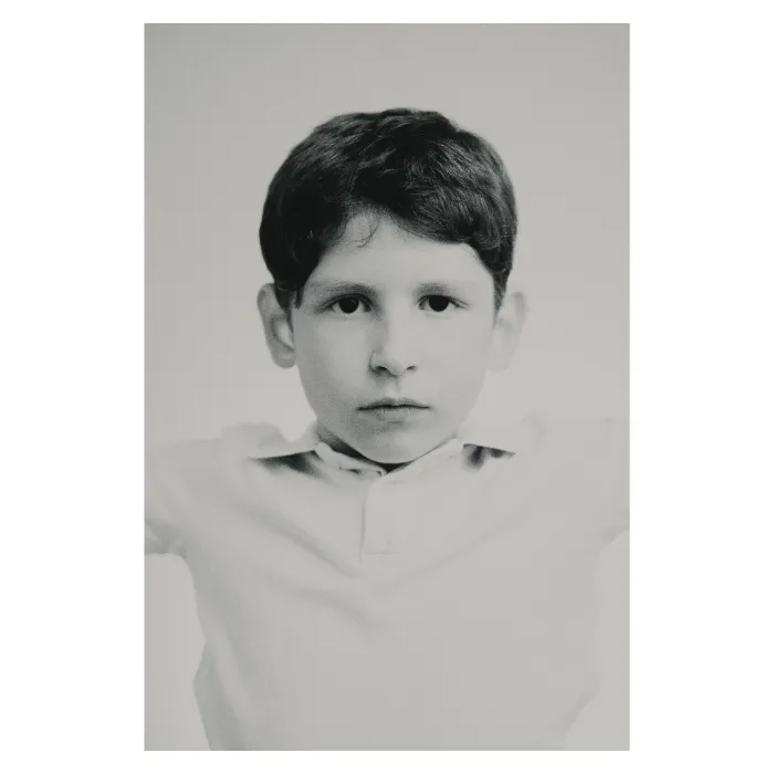 Portrait de face en noir et blanc d'un jeune garçon au regard sérieux et direct, cheveux courts coiffés sur le côté, portant un polo clair, photographie de studio épurée réalisée à Aubervilliers par Nicolas Louis.