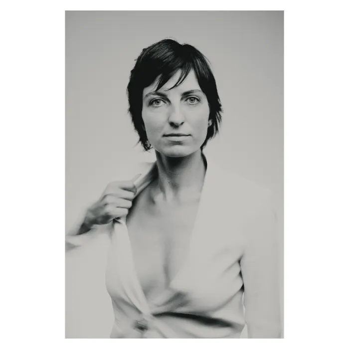 Portrait de face en noir et blanc d'une femme au regard direct, ajustant le col d'une veste de costume blanche entrouverte, coupe de cheveux courte déstructurée, photographie de studio à la lumière douce réalisée à Paris par Nicolas Louis.