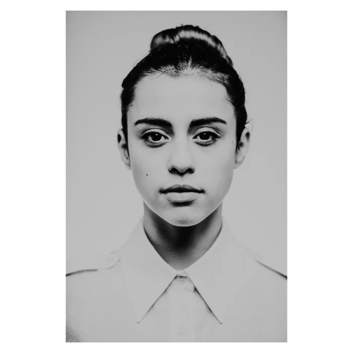 "Portrait de face en noir et blanc d'une jeune femme au regard direct et calme, visage encadré par un chignon haut, portant une chemise blanche boutonnée, esthétique de studio épurée réalisée au Vésinet par Nicolas Louis.