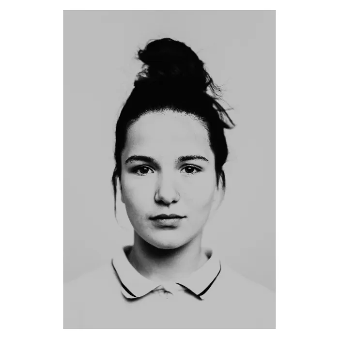 Portrait de face en noir et blanc d'une jeune femme aux yeux clos, visage serein avec un chignon haut et quelques mèches libres, portant un polo à col liseré sombre, photographie de studio minimaliste réalisée au Vésinet par Nicolas Louis.