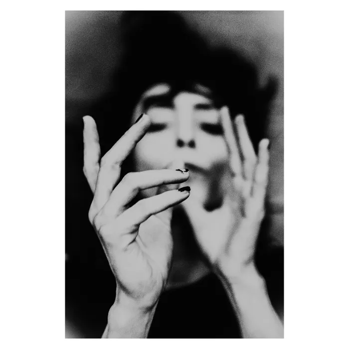 Portrait d'art en noir et blanc avec un flou artistique prononcé, femme aux yeux clos manipulant une cigarette, focus sur la gestuelle des mains et le grain argentique, photographie de studio au Vésinet par Nicolas Louis.