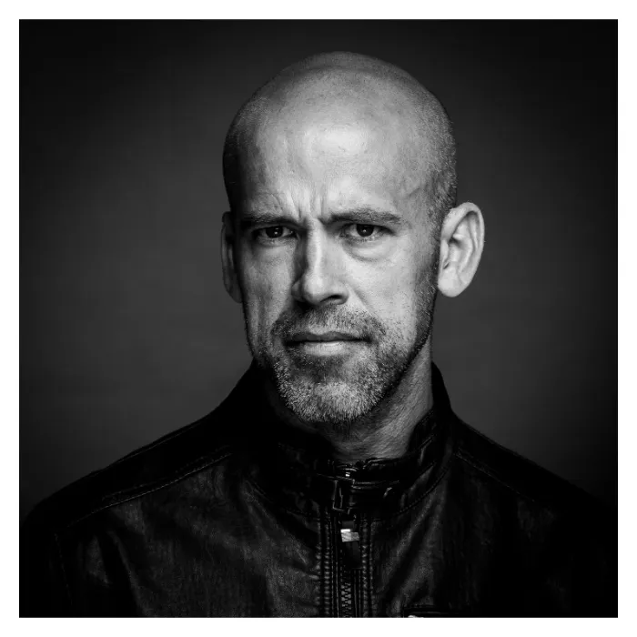 Portrait masculin de face en noir et blanc, homme au regard soutenu et barbe courte portant un blouson en cuir noir, éclairage de studio contrasté, photographie réalisée à Bagnolet par Nicolas Louis.