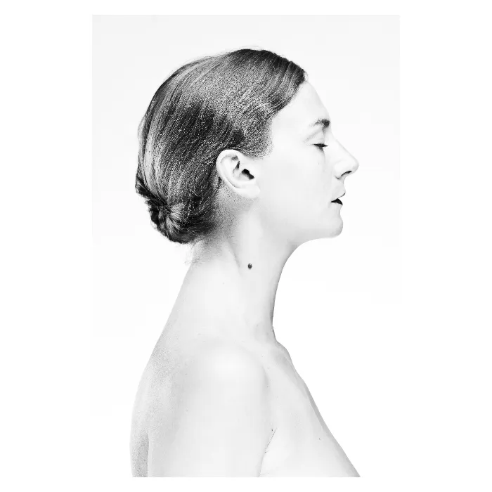 Portrait de profil en noir et blanc de Marthe sur fond blanc immaculé, visage serein aux yeux clos, cheveux coiffés en un chignon bas soigné, esthétique minimaliste et lumineuse (high-key), photographie de studio réalisée à Bagnolet par Nicolas Louis.