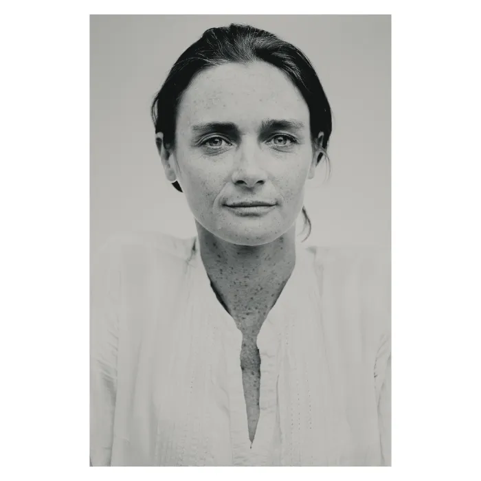Portrait féminin naturel en noir et blanc, femme aux yeux clairs et taches de rousseur portant une chemise blanche, regard frontal doux, photographie de studio réalisée à Paris par Nicolas Louis."