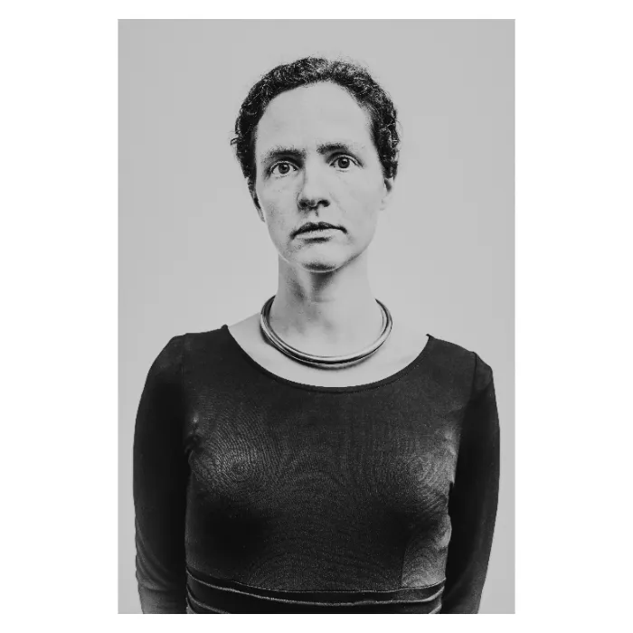 Portrait d'art frontal en noir et blanc d'une femme au regard sérieux portant un collier torque métallique imposant, éclairage studio épuré sur fond gris, photographie réalisée au Vésinet par Nicolas Louis.