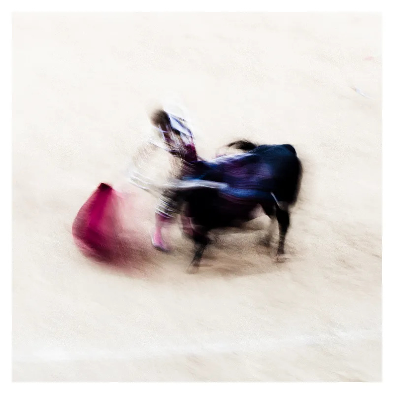 Photographie artistique en flou de mouvement d'un torero effectuant une passe avec sa cape rose, vêtu d'un habit de lumière bleu et or, sur le sable beige de l'arène de Bayonne, style Ernst Haas