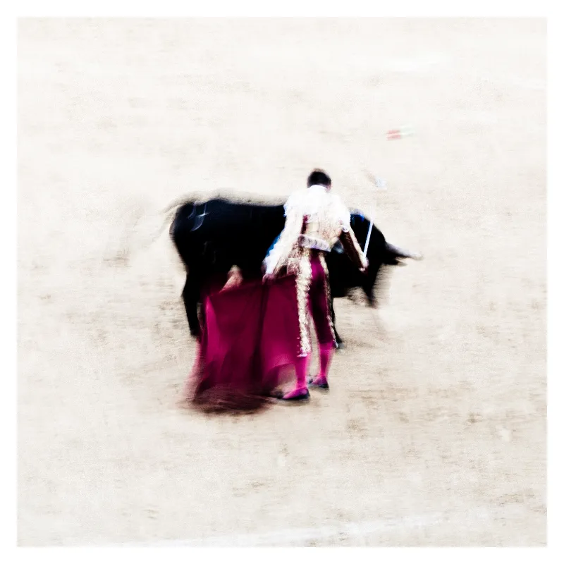 Photographie artistique en flou de mouvement d'un torero en habit de lumière rose fuchsia et noir face à un taureau dans l'arène de Bayonne, texture picturale inspirée d'Ernst Haas
