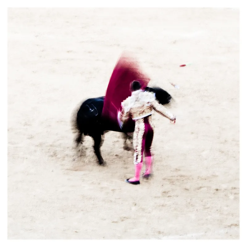 Photographie artistique d'un torero en costume magenta face à un taureau noir dans les arènes de Bayonne, traitement en flou de mouvement inspiré d'Ernst Haas, ambiance impressionniste capturant l'intensité de la corrida