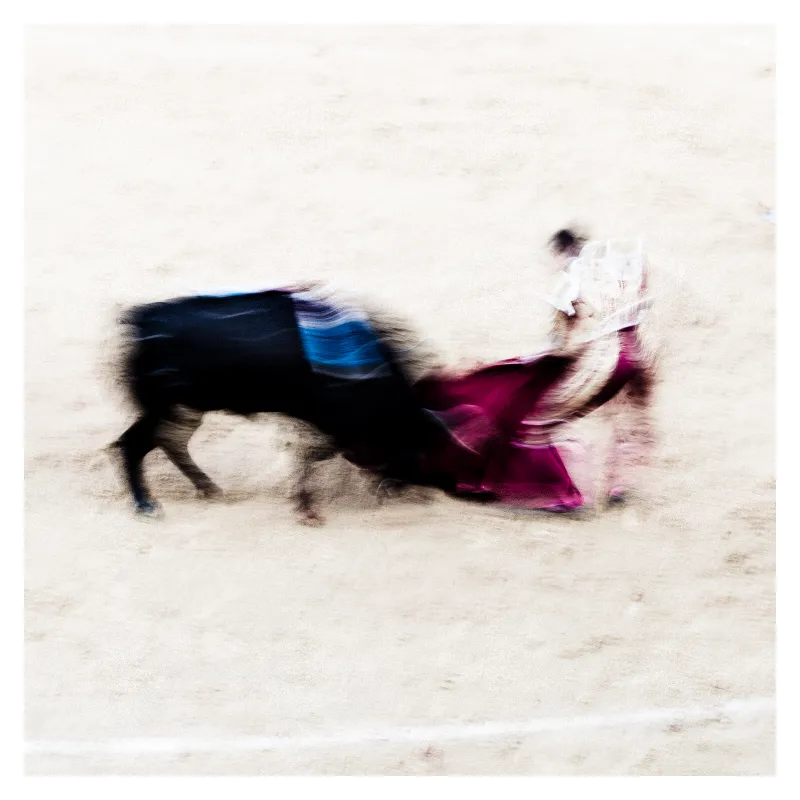 Photographie artistique en flou de mouvement d'un torero maniant sa cape magenta face à un taureau noir, arènes de Bayonne, style Ernst Haas, technique longue exposition créant une abstraction dynamique