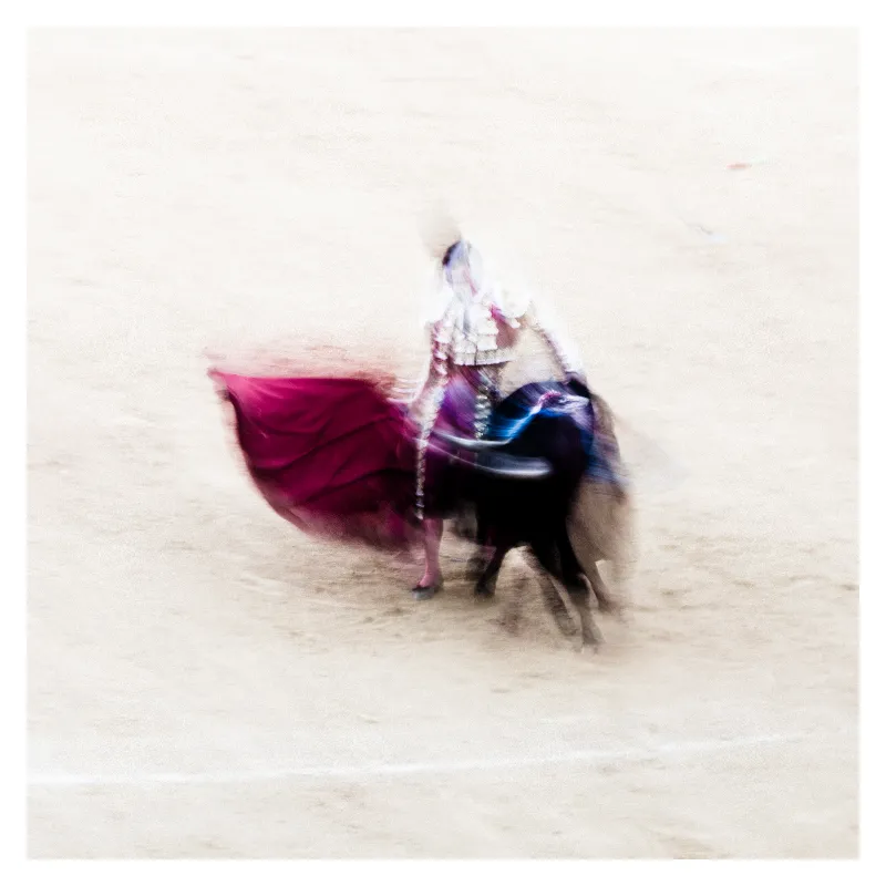 Photographie artistique en flou de mouvement d'un torero affrontant un taureau noir, cape magenta déployée créant une traînée dynamique, technique d'exposition longue inspirée par Ernst Haas, ambiance éthérée sur fond beige lumineux