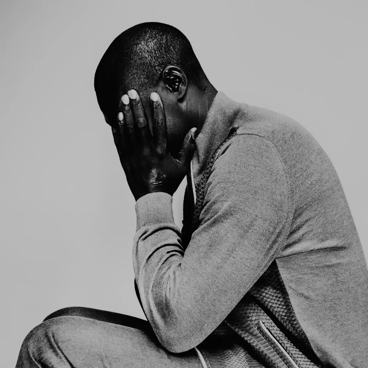 Portrait artistique en noir et blanc dans un studio photo d'un homme, de profil les coudes posés sur les cuisses et la mains apposées sur le visage. Réalisée à bagnolet