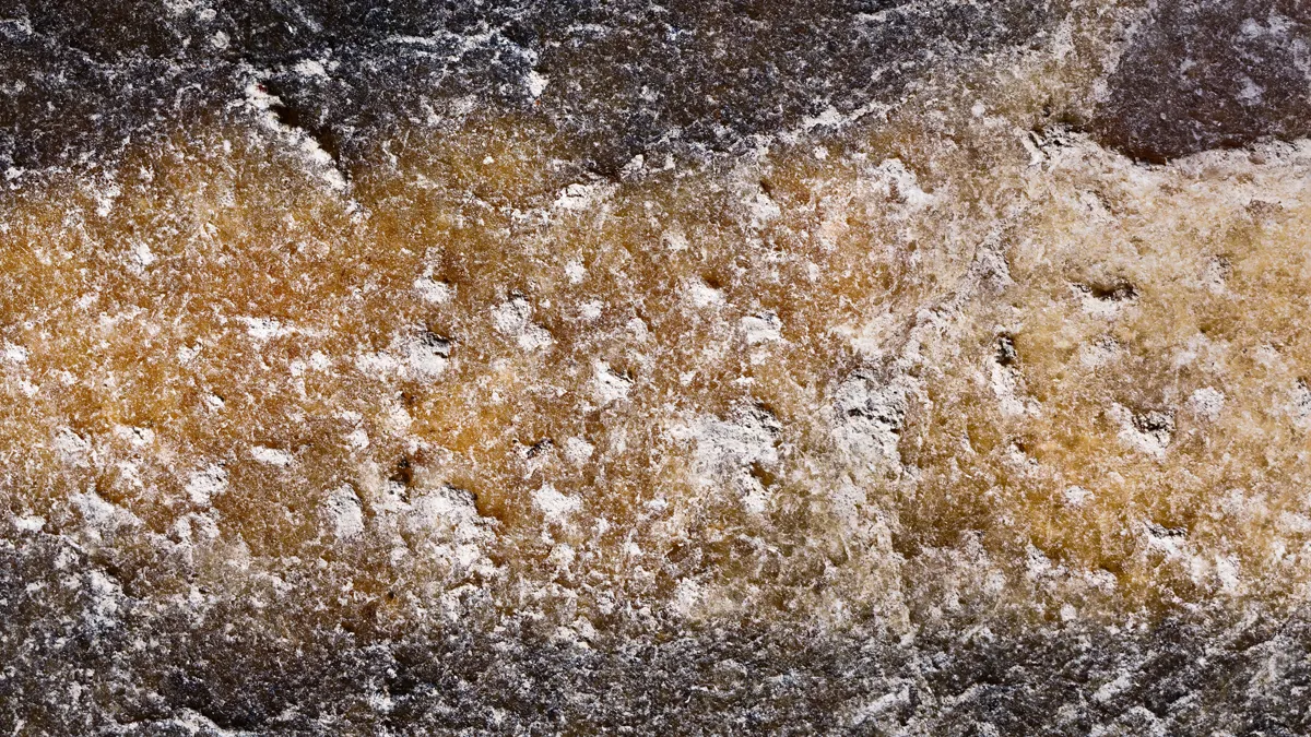 Macro-photographie d'art en studio montrant une bande horizontale texturée d'un brun-jaune ambré et de micro-cristaux blancs, encadrée par une roche granuleuse et sombre d'un noir profond.