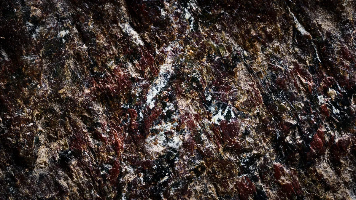 Macro-photographie d'art en studio montrant le détail d'une pierre sombre et rugueuse aux teintes bordeaux et marron foncé, traversée par une traînée centrale d'inclusions cristallines blanches et noires.