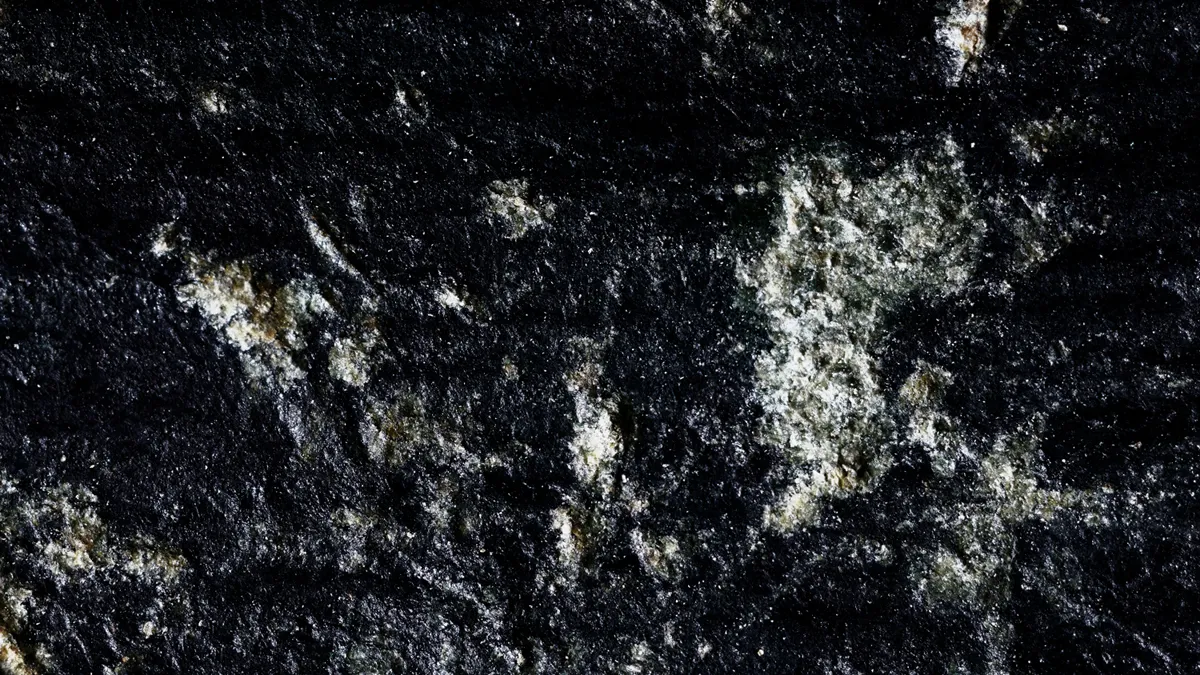 Macro-photographie spectaculaire de studio d'une pierre d'un noir profond, révélant une texture de surface texturée et granuleuse avec des poches d'inclusions cristallines blanches et chatoyantes, rappelant des formations minérales complexes sous un éclairage contrôlé.