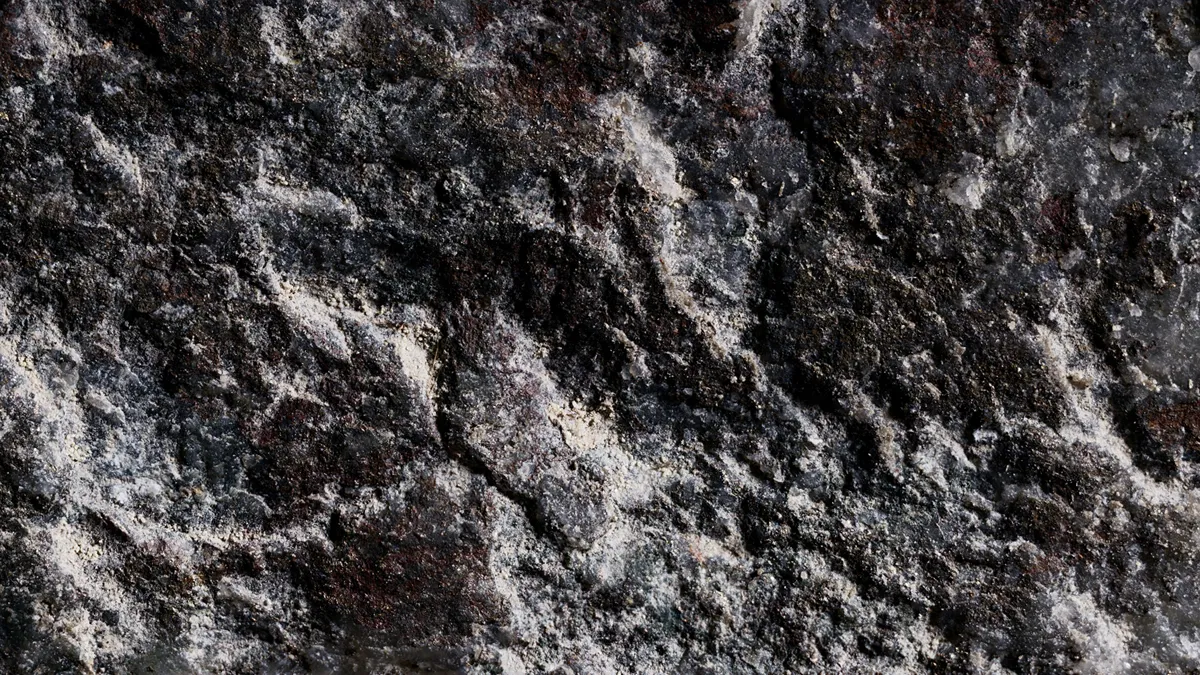 Gros plan de studio à haute résolution d'une pierre granuleuse et texturée d'un noir profond, mettant en évidence des dépôts minéraux texturés et granuleux d'un brun-rouge rouillé et des taches de rouille plus claires et complexes sur une surface texturée.