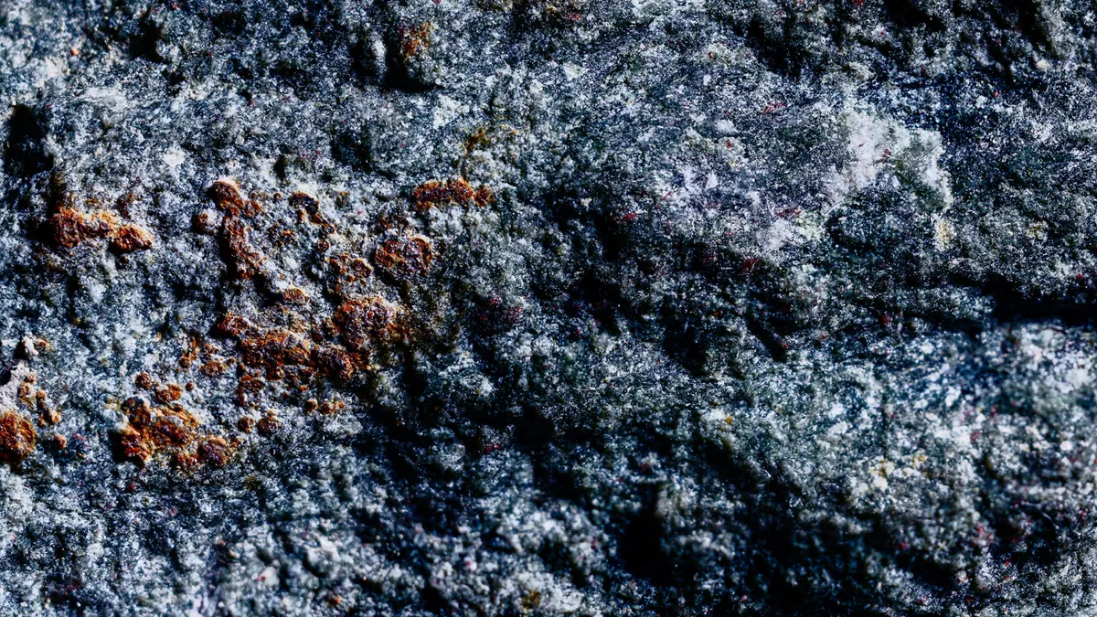 Photographie de studio à ultra-gros plan d'une surface texturée et granuleuse d'une pierre bleu-noir granuleuse et texturée, révélant des micro-cristaux complexes, des variations de couleur texturées et des taches d'un brun profond et granuleuse sous une lumière définie.