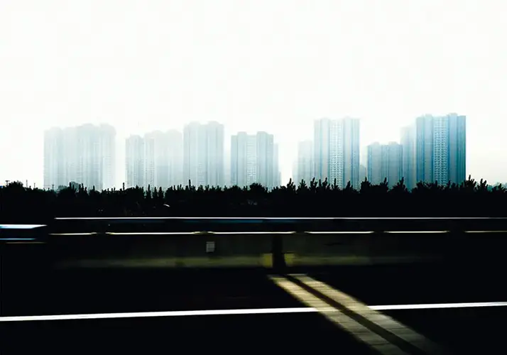 Vue floue du skyline urbain de Pékin depuis une autoroute, capturant l'essence onirique de la ville en mouvement, et de ses zones d’habitation de masses.