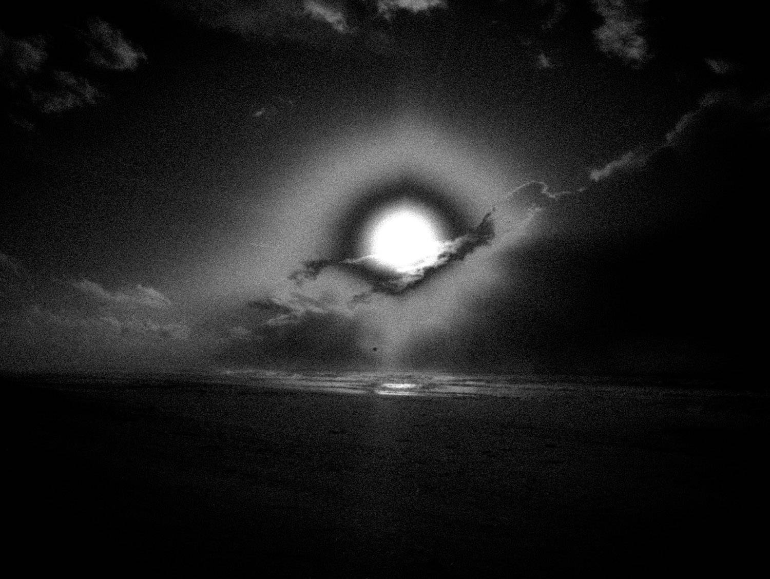 Photographie artistique en noir et blanc d’un paysage cotier désert, avec ciel nuageux et plage balayee par le vent. Style granuleux et minimaliste, evoquant la solitude, le silence et la poesie du littoral.